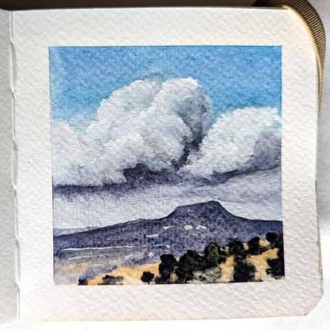 A small watercolor landscape of a distant flat topped mountain under some clouds