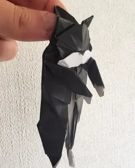A paper model of a cat being held by the scruff of its neck