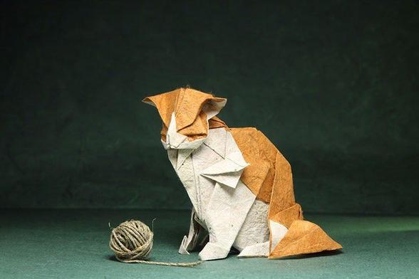 an origami model of a sitting calico cat paired with a small twisted ball of yarn.