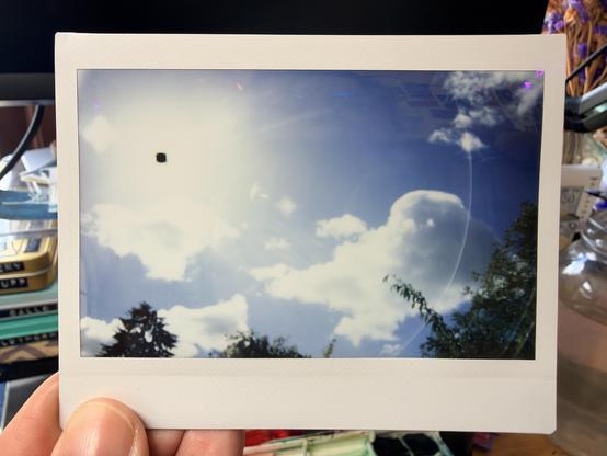 A blue sky, with puffy clouds and a small black dot that is actually the sun.
