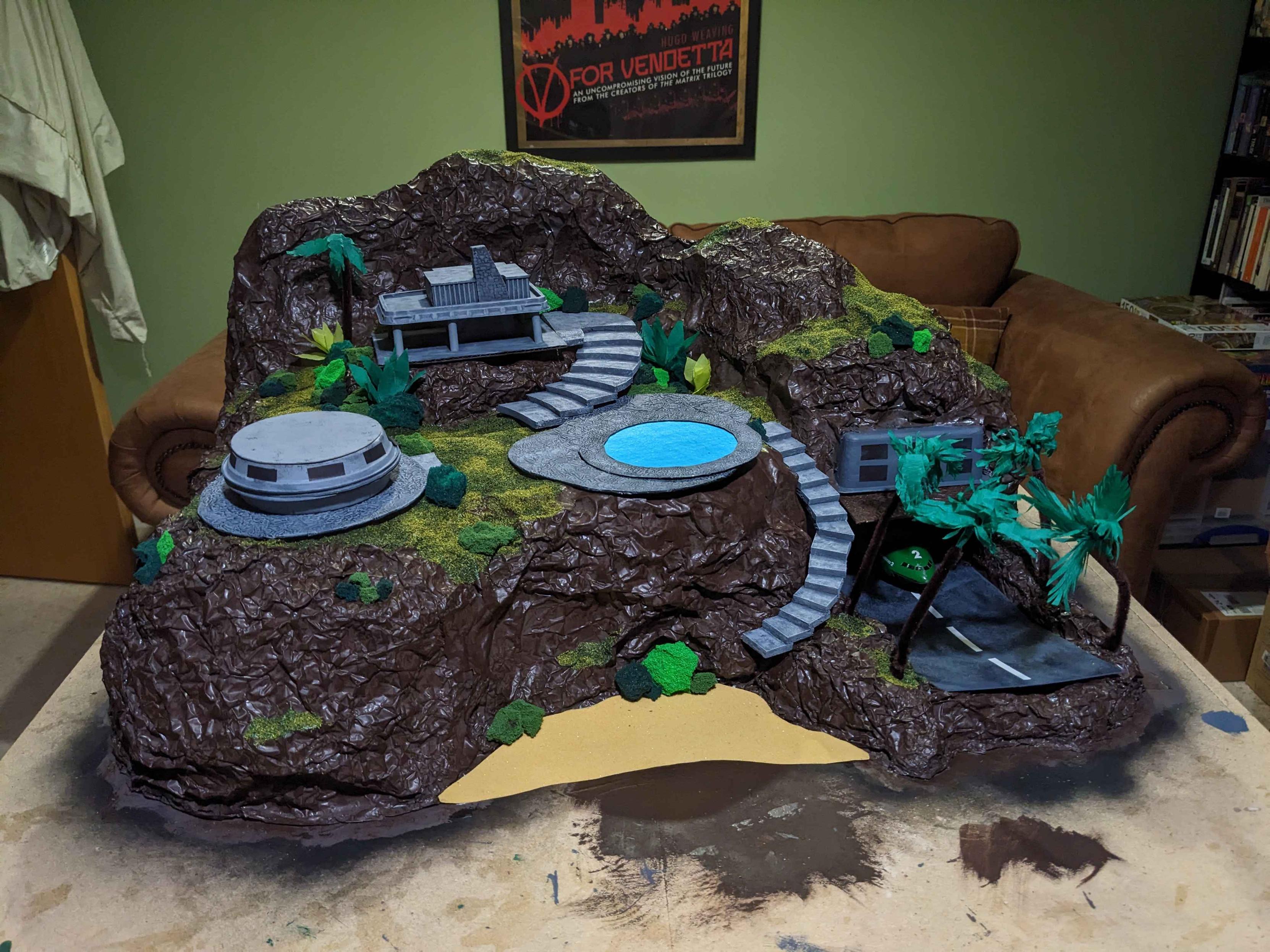 Tracy Island a la Blue Peter has taken form. A photo of an island made from household materials with a swimming pool and two houses on it. There is visible a runway partially hidden behind some pipe cleaner palm trees. There is currently no water so I guess it isn't really an island.