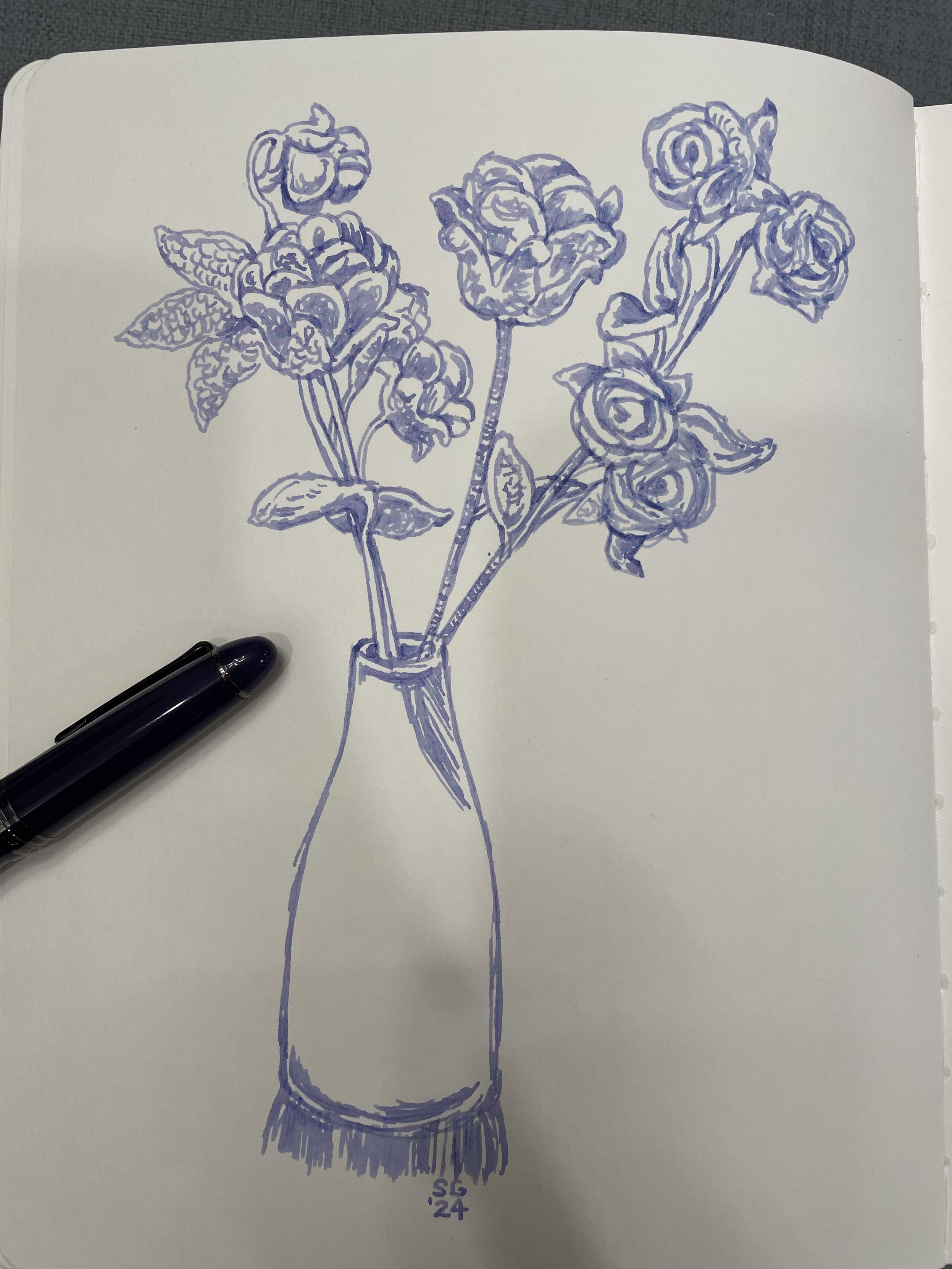 A fountain pen drawing is a vase with fabric roses in it, part of a dark purple fountain pen visible laid across the page. The ink used is a purpley blue.