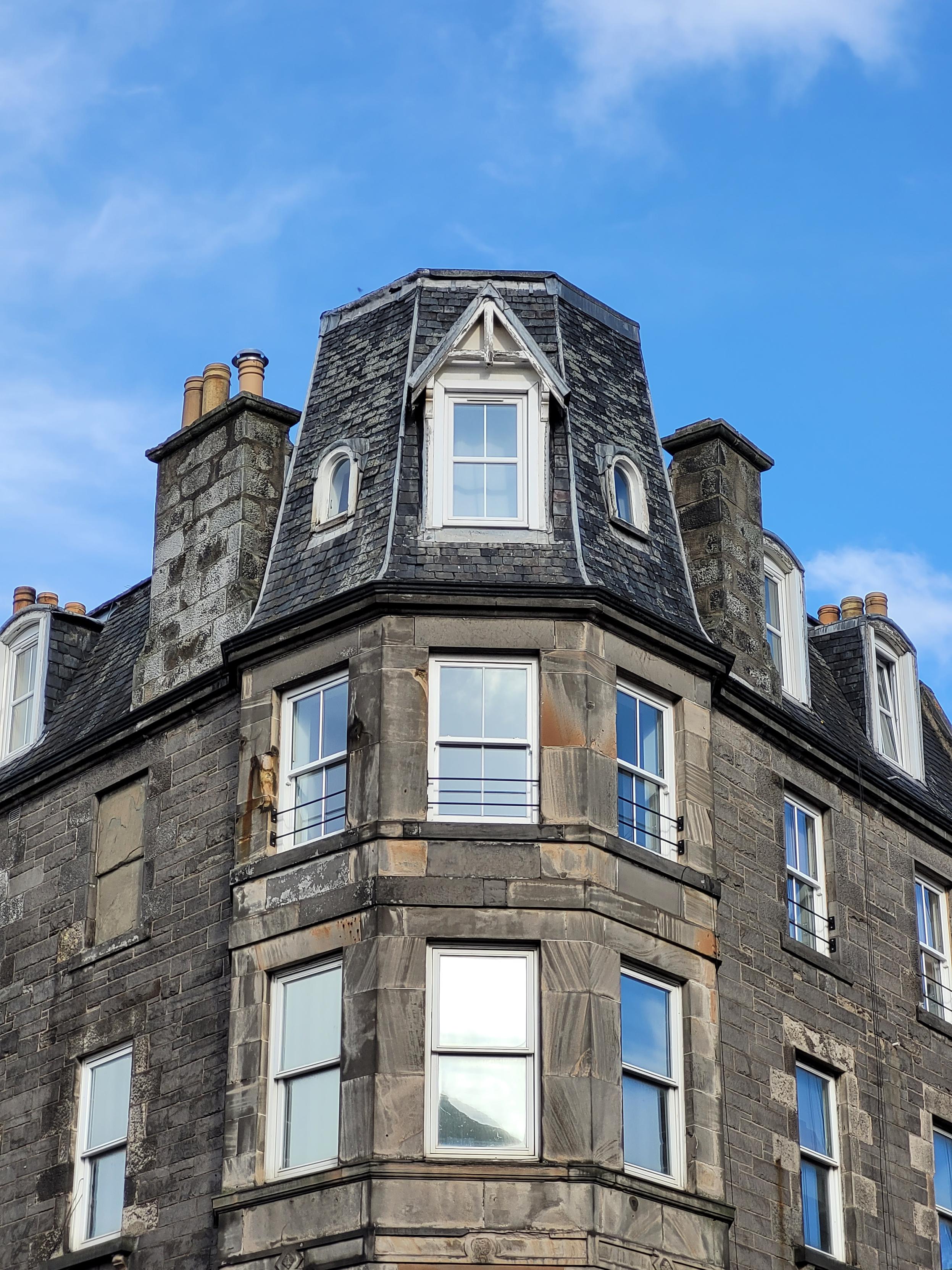 Photograph of the upper floors of an Edinburgh corner tenement building. There is a blue sky above them