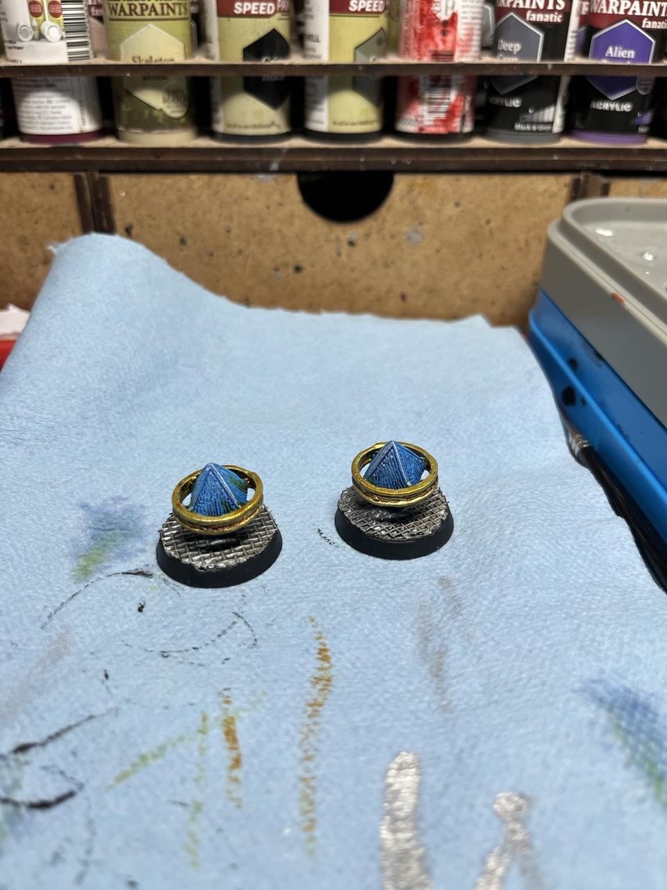 A set of two objectives markers for 28mm sci fi wargaming. They are two floating blue gems with golden rings around them.