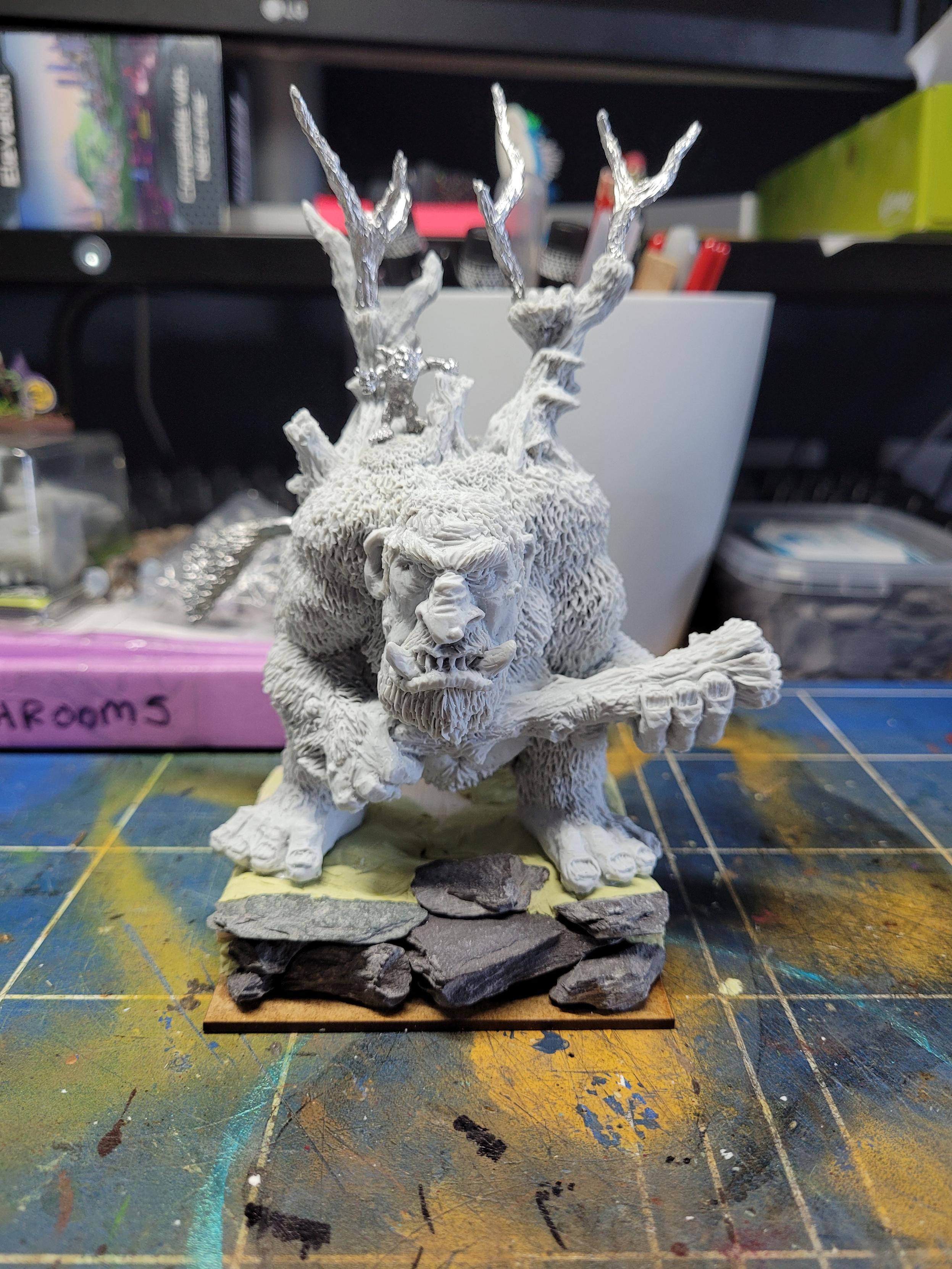 A photo of a large resin troll model. It is holding a tree trunk as a club and has branches growing out of the top of its shoulders. A snotling is standing on top of it, pointing forward as though anyone can control Albert the Forest Troll
