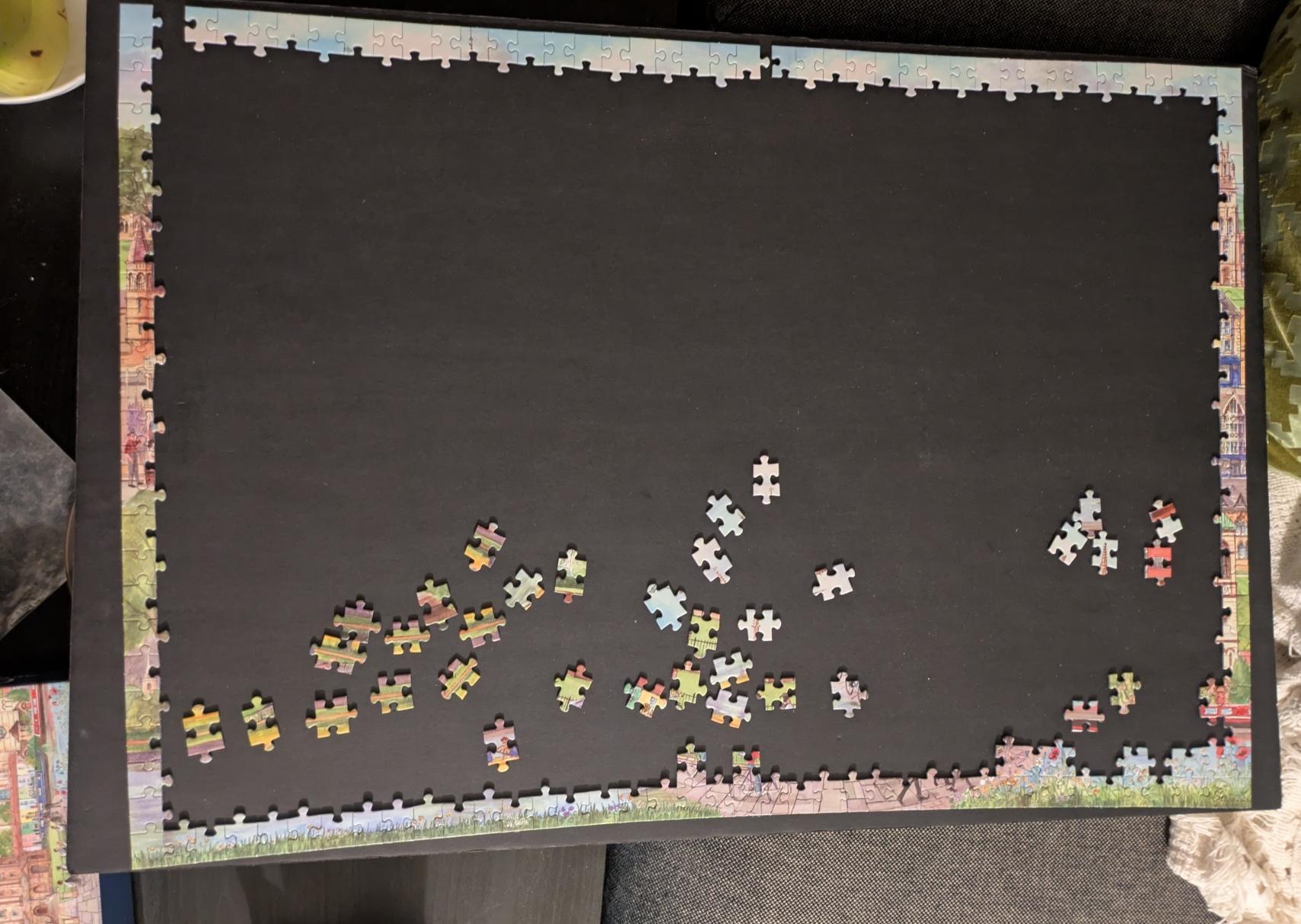 Top down photo of a partially completed jigsaw puzzle on top of a black piece of card board. There are a couple gaps along the top edge but the sides and bottom are complete.